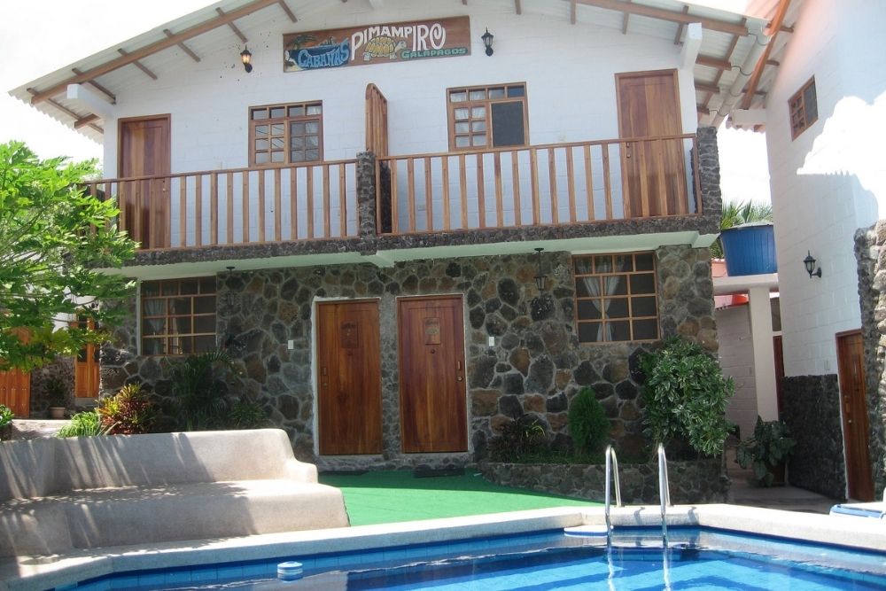 Stone and white exterior of Cabañas Pimampiro in the Galápagos, with wooden balcony and pool