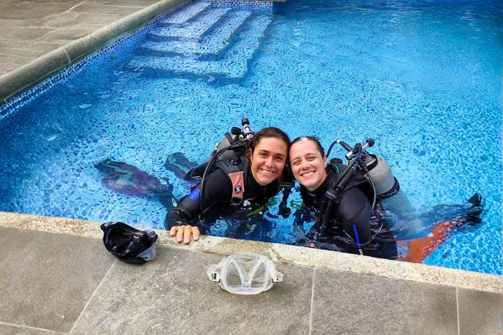 Two smiling divers resting at the edge of a swimming pool during a learn to dive in galapagos course in Puerto Ayora