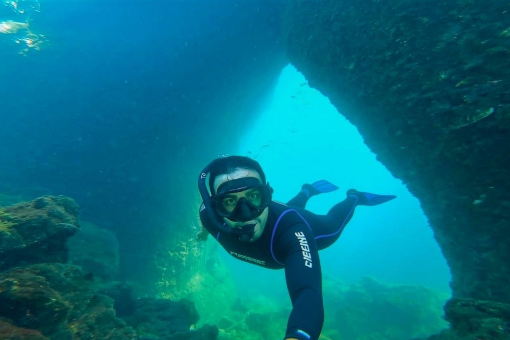 Snorkeler swimming under underwater volcanic rock arches at Los tuneles on an active Galapagos Multisport tour