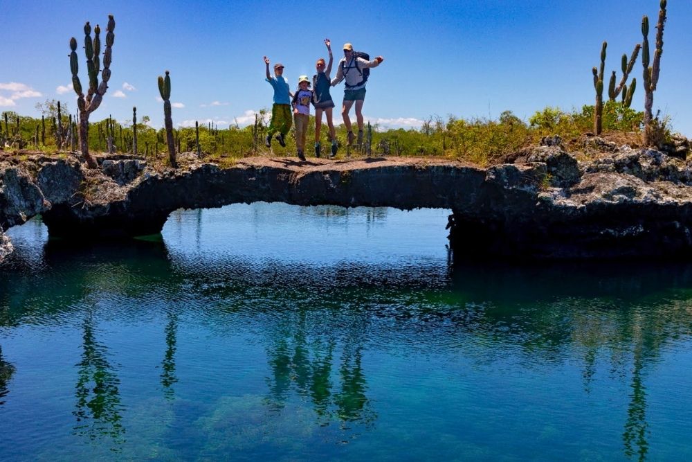 Family jumping in the air on a natural lava bridge above turquoise water at sites like kicker rock los tuneles