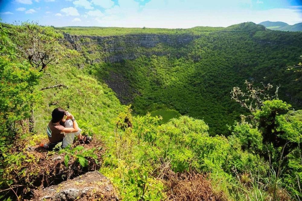 Hiker taking in the view of a lush green sinkhole at the twins craters on a short ecuador galapagos tour itinerary
