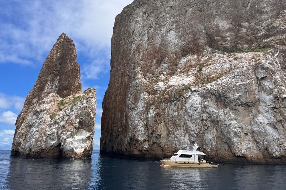 Luxury yacht cruising past the dramatic vertical rock cliffs of Kicker Rock during a private galapagos tour excursion