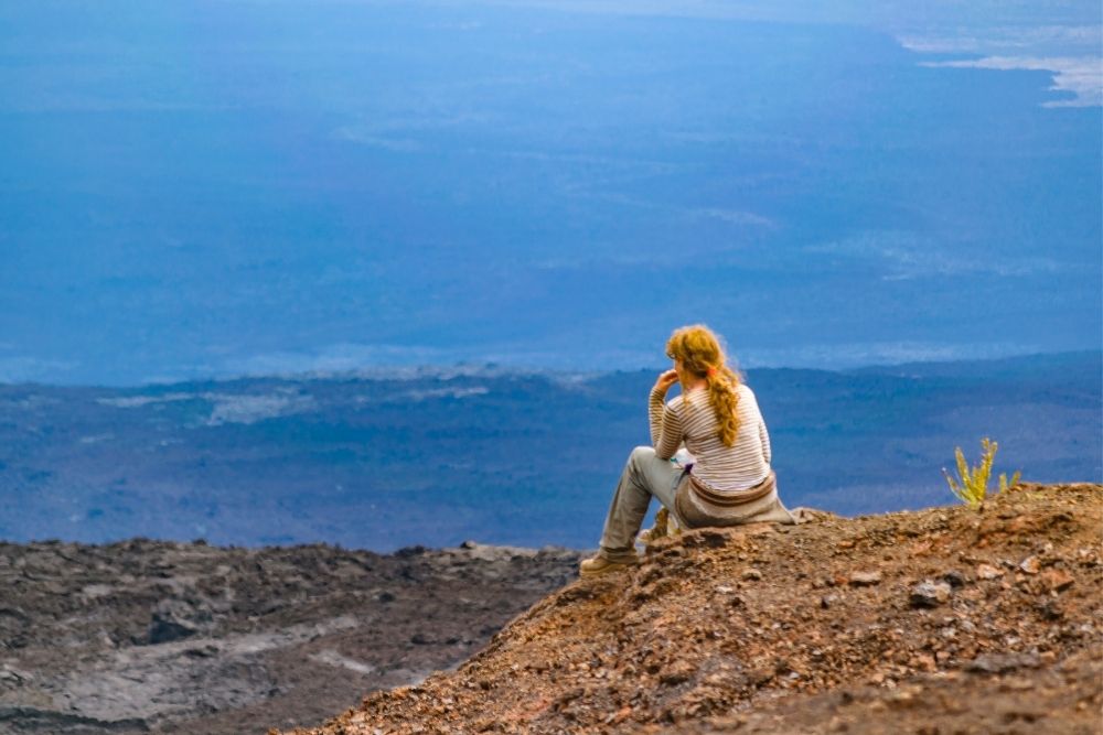 A traveler sitting on a crater rim overlooking lava fields at Sierra Negra during a galapagos island hopping 6 days tour