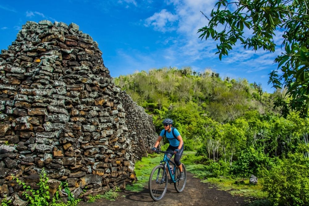 A cyclist riding a bicycle along a dirt path next to the historic Wall of tears Isabela in the Galapagos Islands