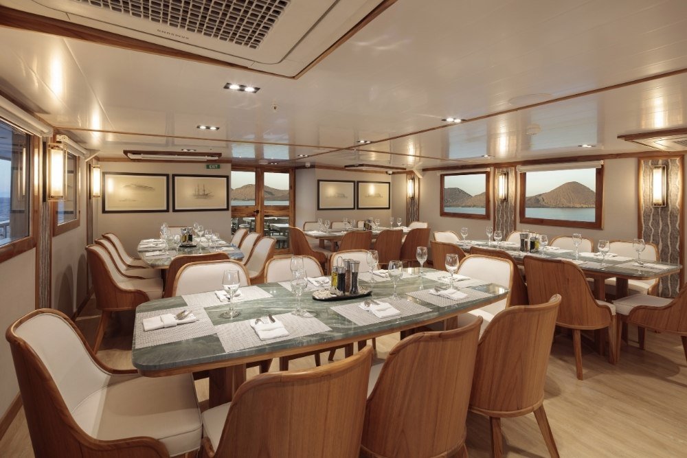 elegant dining room on an evolution galapagos cruise featuring marble tables and wood chairs with ocean views.
