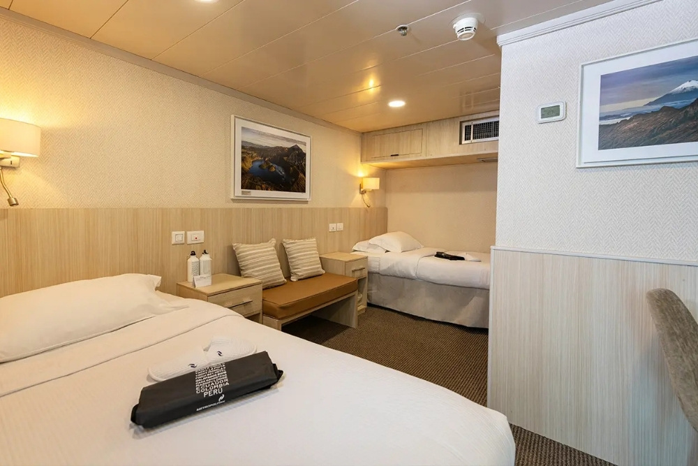 cozy twin stateroom with warm lighting and framed artwork on the isabela ii galapagos cruise.