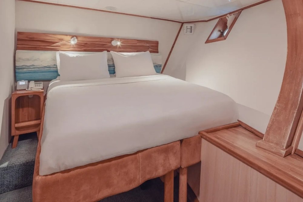 A cozy double bed cabin with a classic ocean porthole aboard the Coral Yachts.