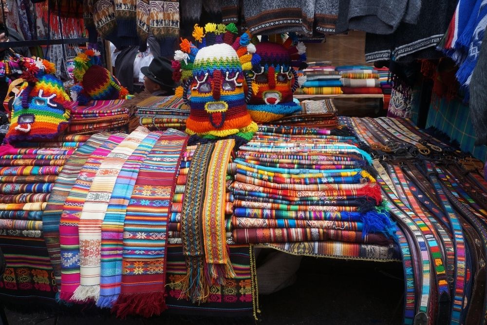 Colorful textiles and handmade crafts displayed during an Otavalo market tour at Plaza de los Ponchos