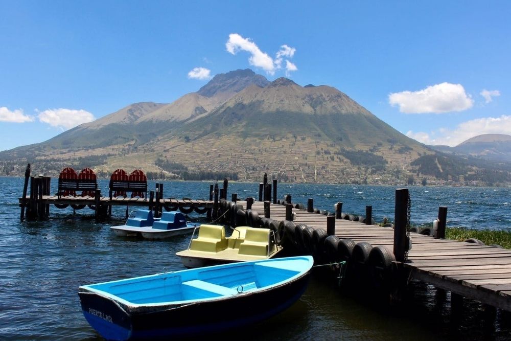 View of San Pablo Lake in Otavalo with boats, a wooden dock, and Imbabura volcano in the background