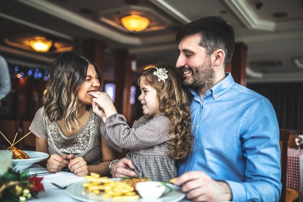 parents and child laughing and sharing food during a family lunch at a cozy restaurant table