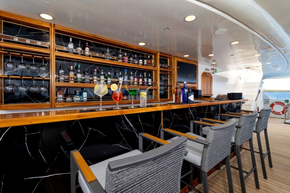 A sleek outdoor bar on the upper deck of the Galapagos Horizon luxury trimaran lined with modern bar stools, marble finishes, and colorful tropical cocktails ready for guests.