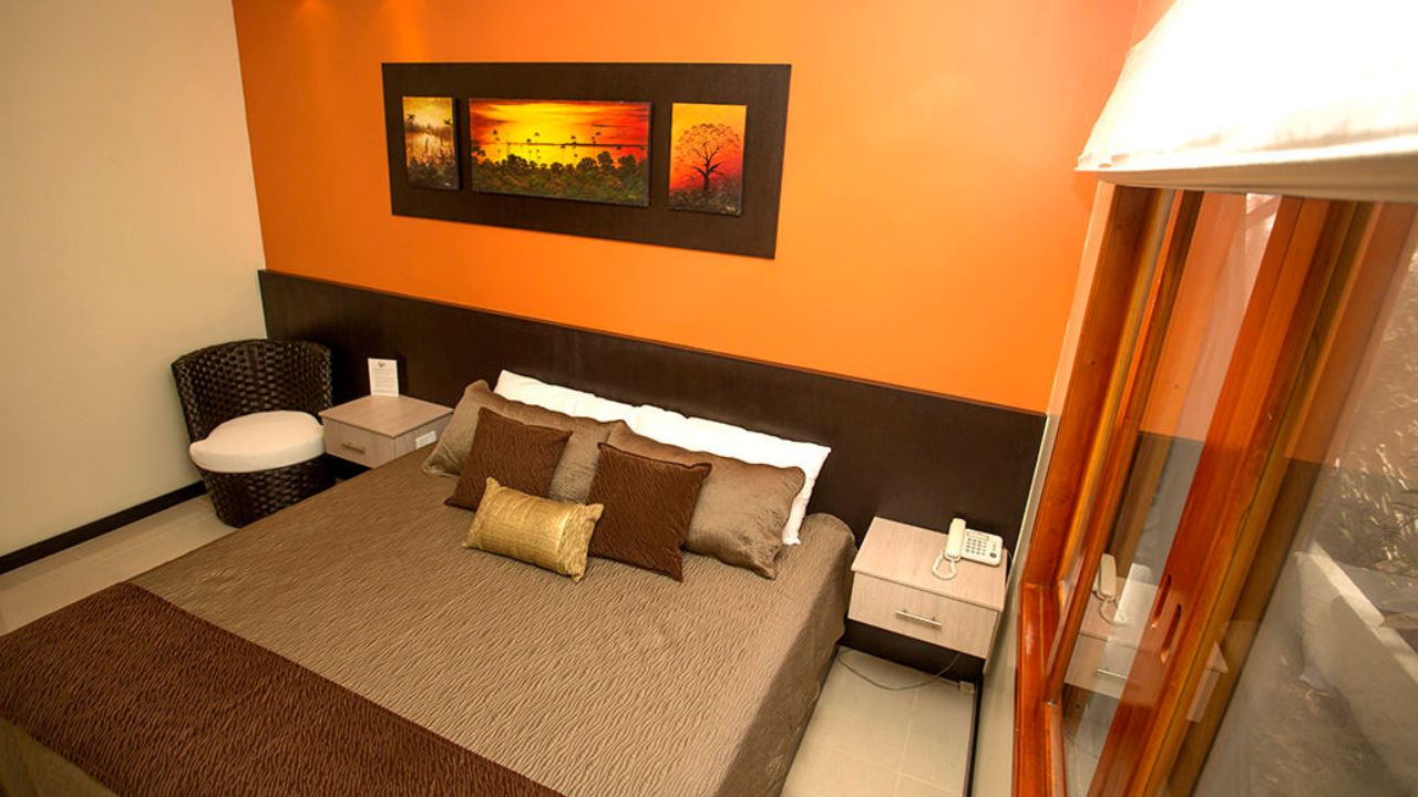 A modern hotel room featuring a bed with neutral linens and vibrant orange walls at Hotel La Laguna in Galapagos