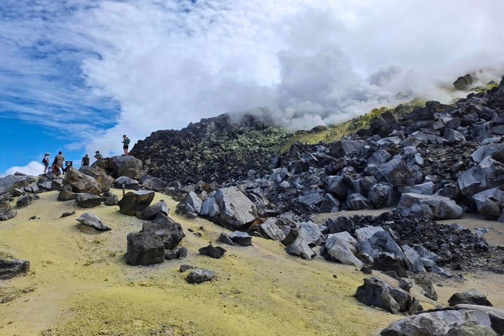 Hikers standing near smoking steam vents and volcanic rocks at Sierra Negra Sulfur Mines on Isabela Island Galapagos