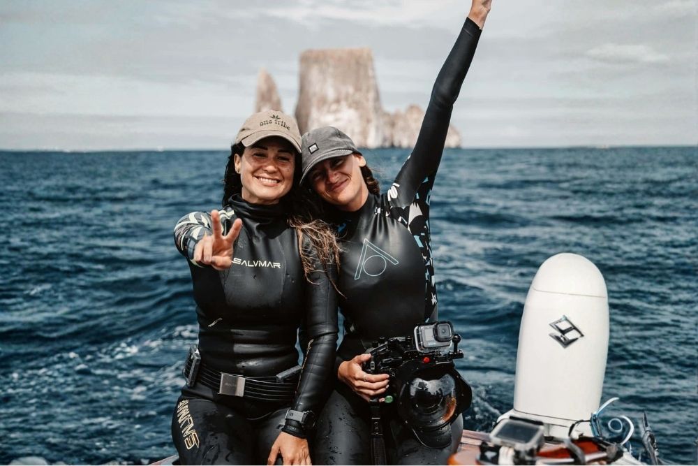 Two female divers celebrating on a boat in front of Kicker Rock during an 8 day women Galapagos snorkeling excursion