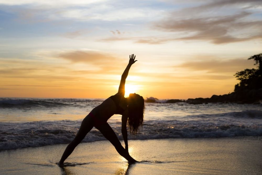 Woman practicing a yoga triangle pose in silhouette at sunset along the shore during a Galapagos Yoga Tour Tortuga Bay