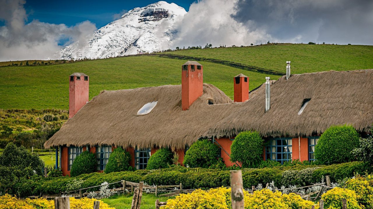 Traditional thatched-roof estate house at Hacienda El Porvenir set against rolling green hills and a snowcapped peak