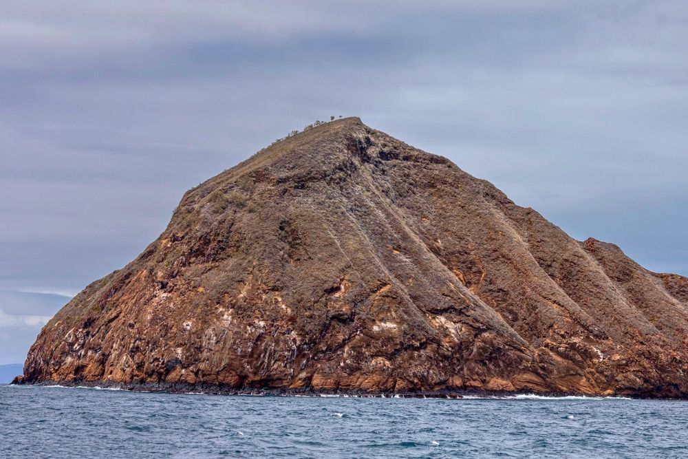 Rocky volcanic islet rising steeply from open ocean waters during a day cruise on a Pinzon Tour in Galapagos Islands