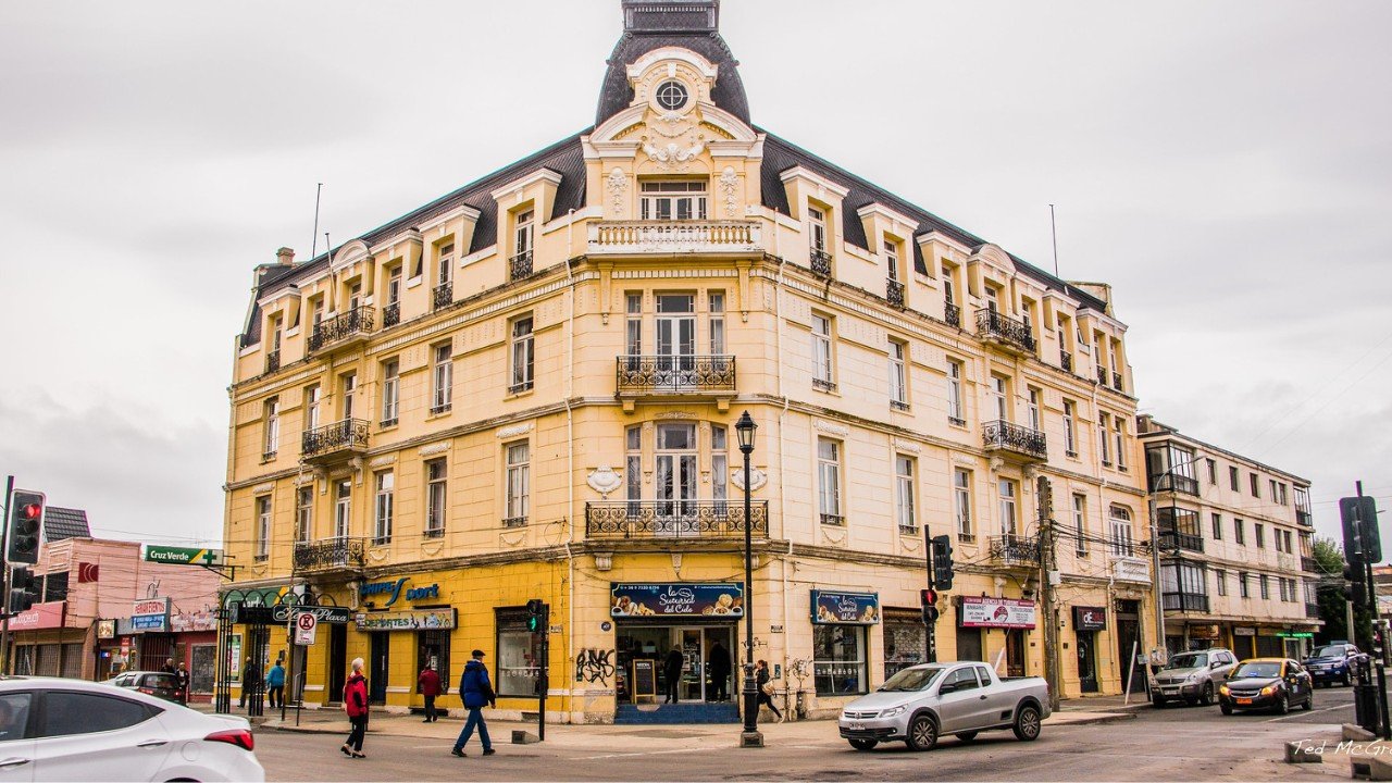 Grand yellow colonial corner facade of Hotel Plaza Punta Arenas overlooking city streets under soft overcast skies
