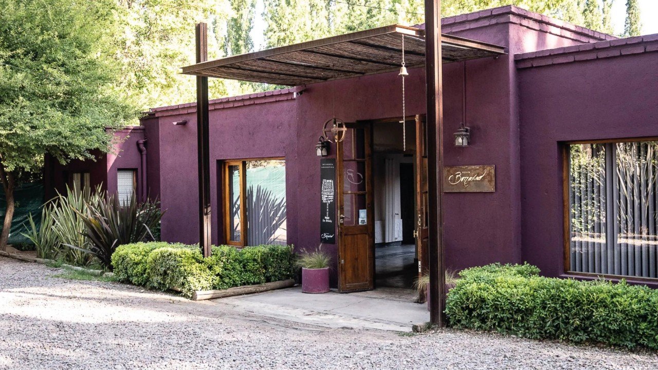 Rich plum facade and wooden pergolas framed by lush green foliage at Posada Barrovino boutique lodge in Mendoza winery