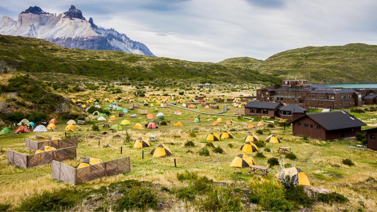 Colorful tents pitched on grassy fields near mountain huts at Refugio & Camping Vertice Paine Grande in Torres del Paine