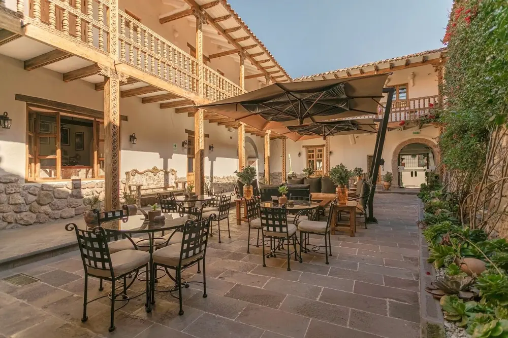 Sunlit stone courtyard with patio dining tables and traditional wooden balconies at Antigua Casona San Blas in Cusco