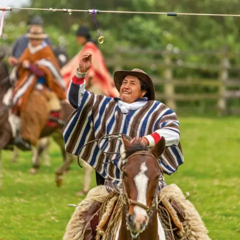 Chagra-Skill Rebecca Adventure Travel A traditional Ecuadorian chagra riding a horse and catching a ring mid-air to demonstrate chagra skills during a local festival.