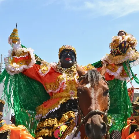 Mama-Negra-Celebration Rebecca Adventure Travel A person dressed as the Mama Negra on horseback wearing a colorful costume and traditional mask during the Mama Negra parade.