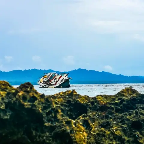 puerto-viejo-talamanca Rebecca Adventure Travel Sunken boat resting in coastal waters framed by dark shoreline rocks in Puerto Viejo Talamanca under blue skies