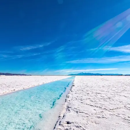 Salt-Lake-argentina Rebecca Adventure Travel A long, straight turquoise water channel cuts through the brilliant white crust of the Salinas Grandes under a vivid blue sky during a Salt lake Argentina drive.