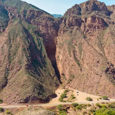 Salta-Devil-throat Rebecca Adventure Travel A massive, narrow red rock crevice known as the Devil's Throat towers over a roadside parking area with several cars during an Argentina Family Drive.