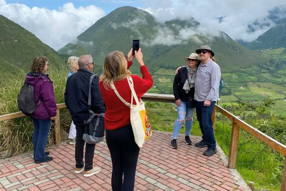 Tourists taking photos at a scenic mountain overlook facing clouds and volcanic hills in Pululahua Ecuador