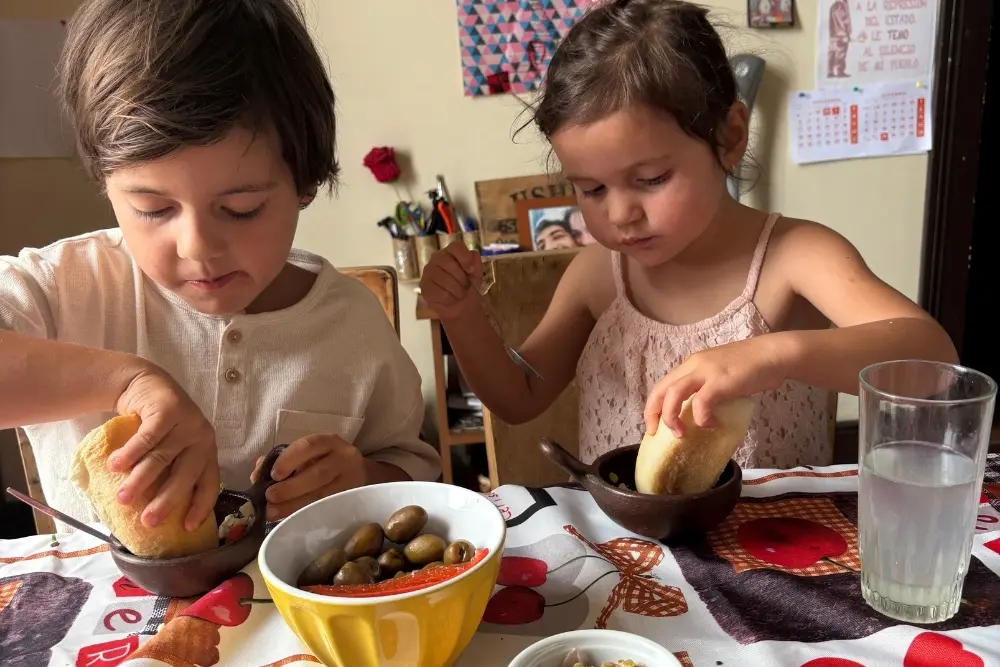 two children dip bread into bowls during a chile family trip cooking class. their table has olives and drinks.