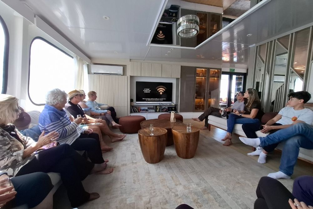multi generational family group relaxing in the lounge of a galapagos cruise ship during a briefing session, highlighting a galapagos cruise for families of all ages