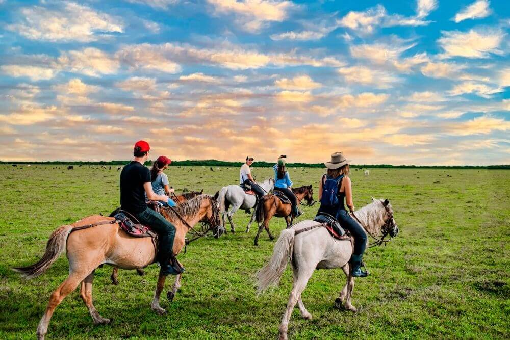 Travelers enjoying a horseback ride during the Colombia Savannah Safari Tour, with a beautiful sunset backdrop.