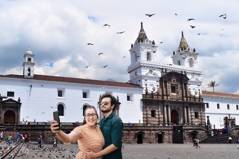 Couple taking a selfie in front of a historic white church with birds flying during a Quito and Galapagos Itinerary