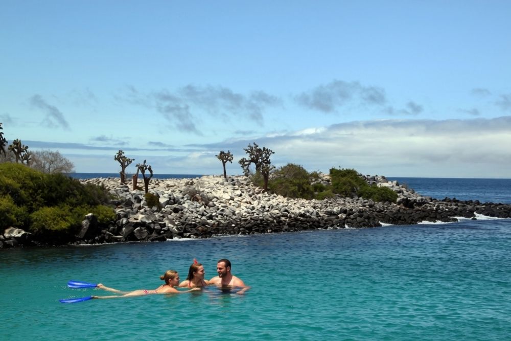 Snorkelers swimming in turquoise cove off a rocky coast on a Santa Fe Ecuador and Galapagos itinerary excursion