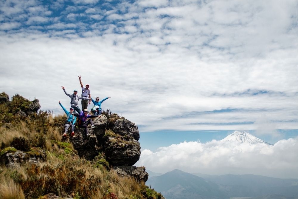 group celebrating on a rocky cliff during a mountain trekking adventure with a snow-capped volcano background