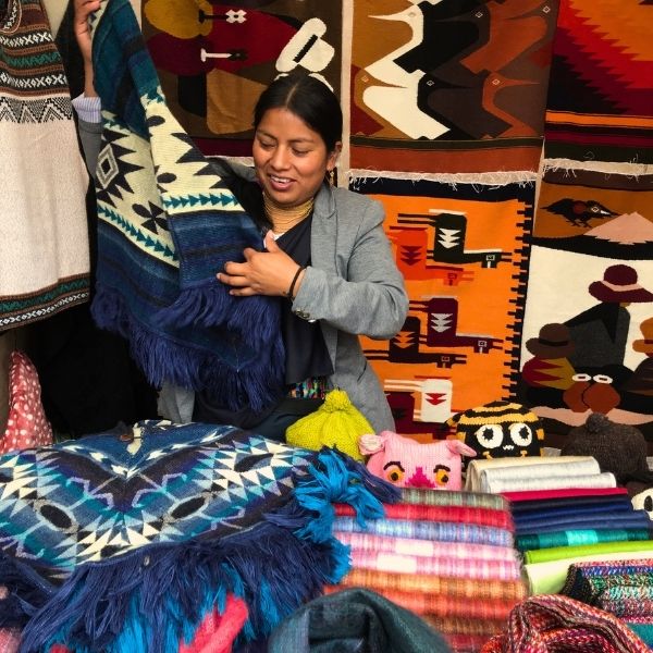 otavalo-market-traditional-textiles-plaza-de-los-ponchos Rebecca Adventure Travel Local artisan displaying colorful handmade textiles and woven ponchos at Otavalo Market in Plaza de los Ponchos